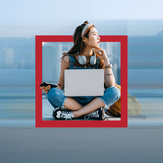 A woman sitting down with a laptop on her lap and a mobile phone in her right hand