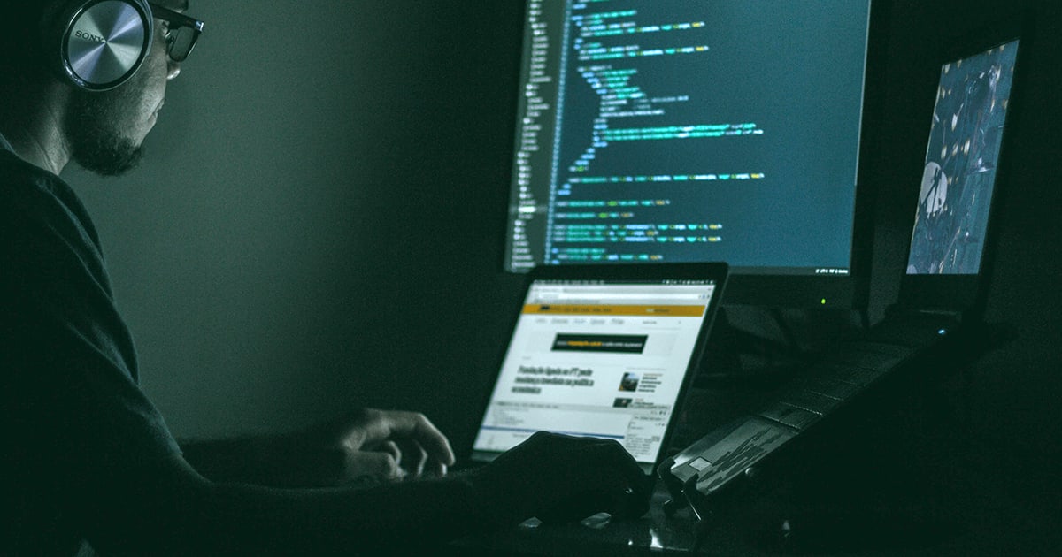 man with headphoes on looking at several computer screens